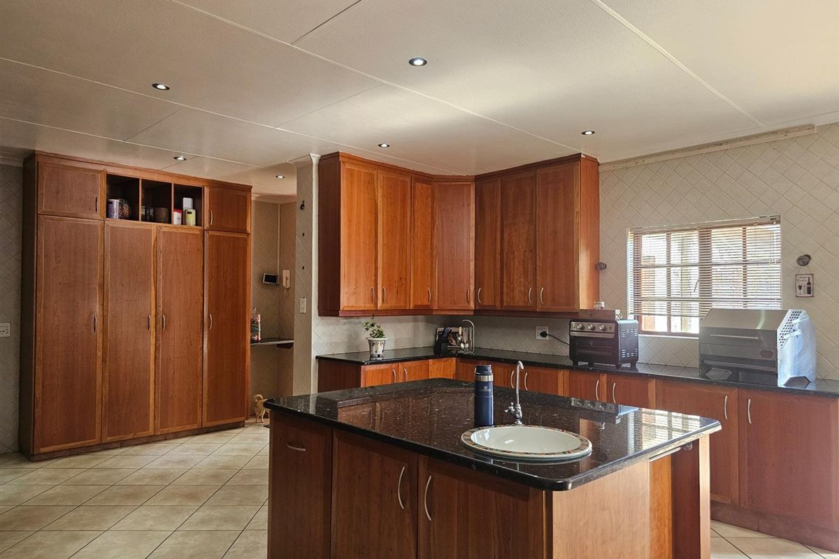 Spacious kitchen featuring extensive wooden cabinetry, a central island with a prep sink, granite countertops, and recessed ceiling lighting.