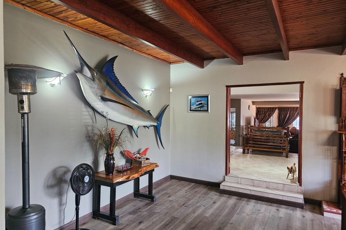 Spacious living area featuring a high timber-beamed ceiling, wood-look flooring, and a step-down transition into an adjoining room.