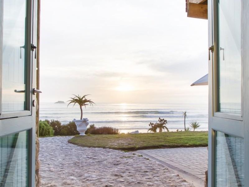 A scenic view of the ocean framed by a rustic stone archway and timber-beamed entrance, leading out to a stone-paved garden path.