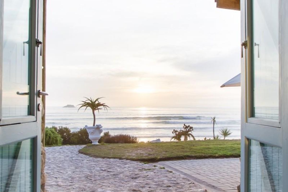 A scenic view of the ocean framed by a rustic stone archway and timber-beamed entrance, leading out to a stone-paved garden path.
