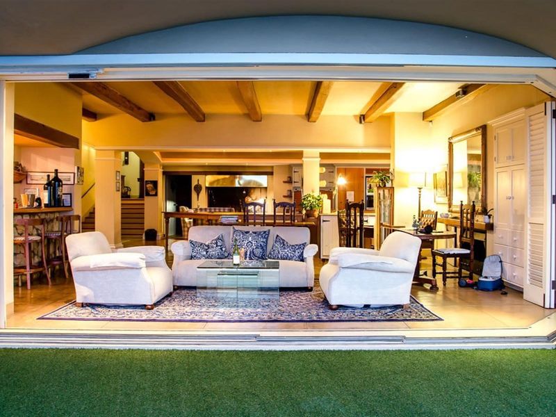 Spacious open-plan living area featuring exposed timber beams, tiled flooring, and seamless indoor-outdoor flow through large stacking glass doors to the garden.
