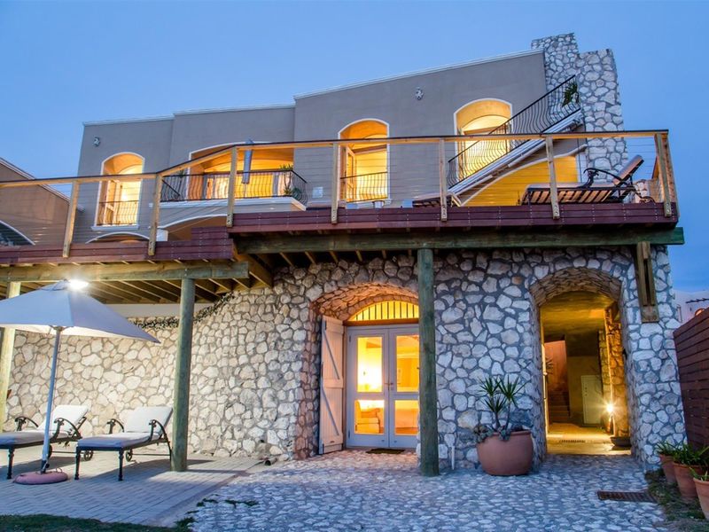 Rear elevation featuring a stone-clad ground level, expansive timber deck with balcony, and arched access points to the interior living spaces.