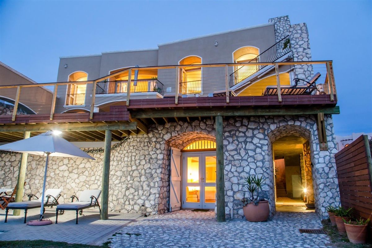 Rear elevation featuring a stone-clad ground level, expansive timber deck with balcony, and arched access points to the interior living spaces.