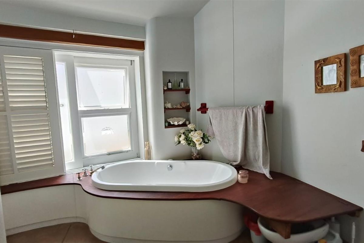 A bathroom featuring a built-in bathtub with a timber surround, recessed wall shelving, and plantation shutters.