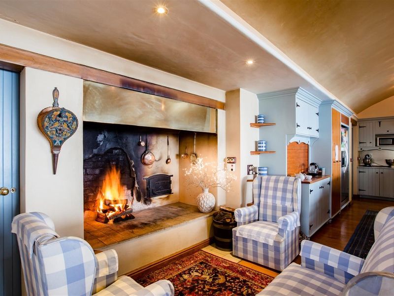 A cozy open-plan living area featuring a large traditional masonry fireplace, timber flooring, and integrated kitchen cabinetry with built-in appliances.