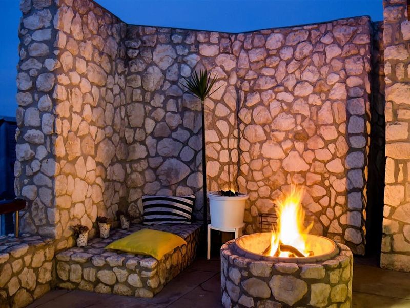 An inviting outdoor patio area featuring a rustic stone masonry wall, built-in stone seating, and a central stone fire pit.