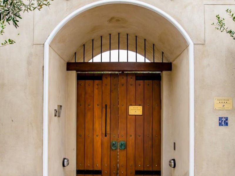 A charming arched entrance featuring solid timber double doors, set within a textured plaster facade and a stone-paved pathway.
