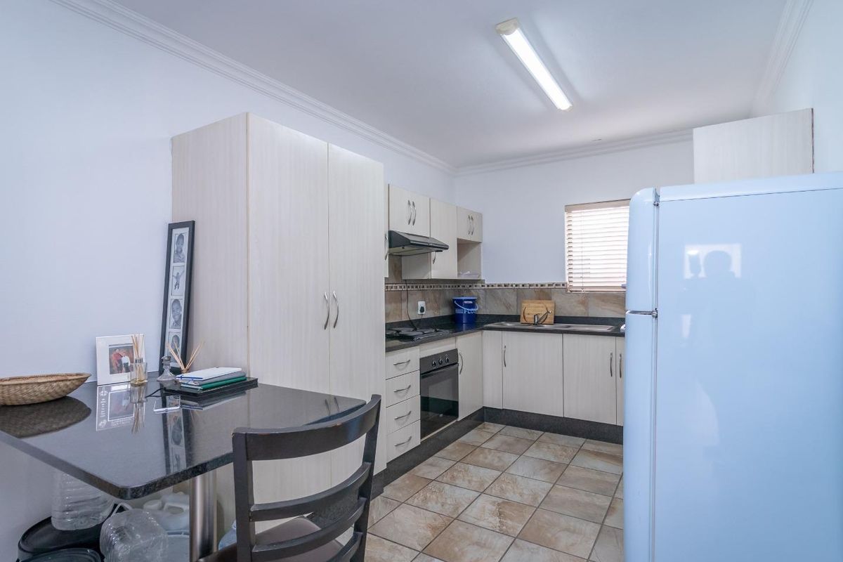 A functional kitchen featuring light-toned cabinetry, dark granite countertops, tiled flooring, a built-in oven, and a hob with an extractor fan.