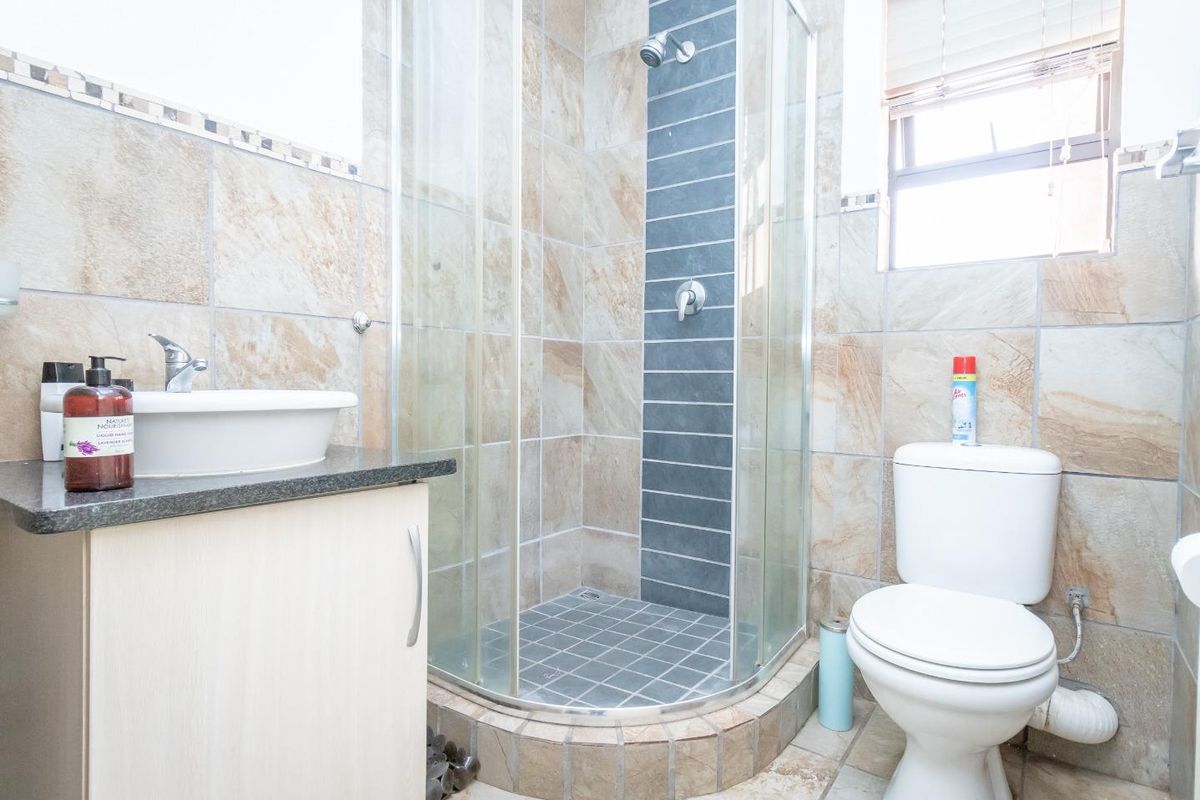 A functional bathroom featuring a corner glass shower enclosure, a vanity with a vessel sink, and a standard toilet with tiled walls and flooring.