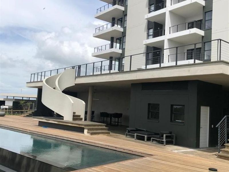 Modern apartment complex pool area featuring timber decking, a striking spiral staircase, and multi-level balconies with metal railings.