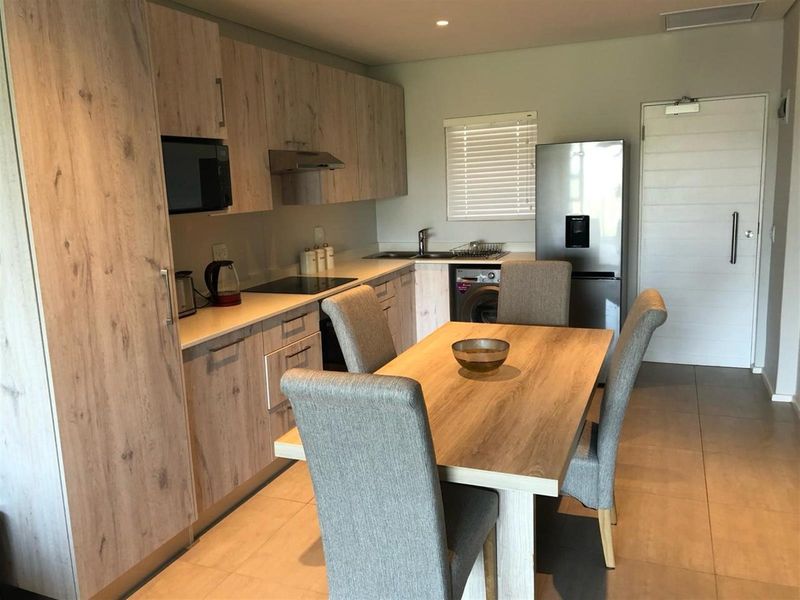 Modern open-plan kitchen featuring light wood-grain cabinetry, stone countertops, integrated appliances, and tiled flooring, seamlessly flowing into the dining area.