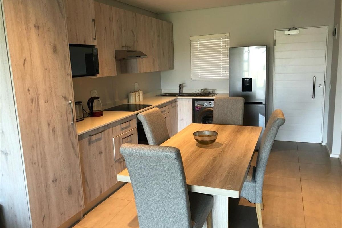 Modern open-plan kitchen featuring light wood-grain cabinetry, stone countertops, integrated appliances, and tiled flooring, seamlessly flowing into the dining area.