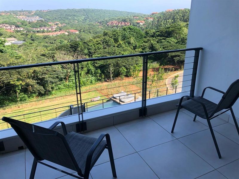 A private balcony featuring tiled flooring and a modern metal balustrade, offering expansive views of the surrounding landscape and greenery.