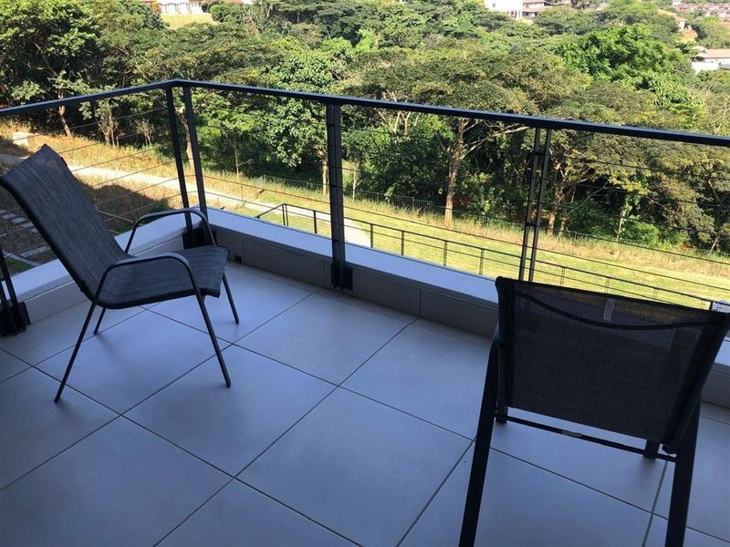 A private balcony featuring modern tiled flooring and a sleek metal balustrade with wire railing, offering elevated views of the surrounding greenery.
