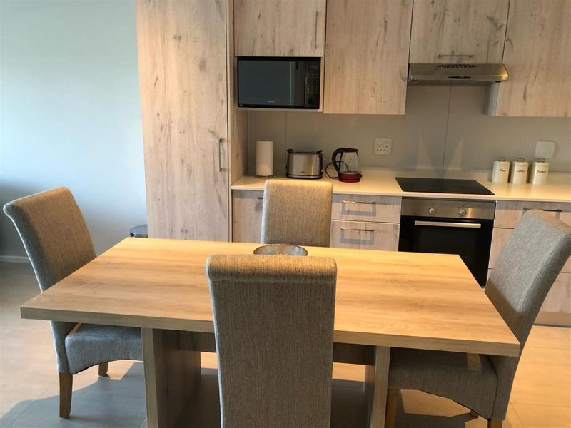 Modern open-plan kitchen featuring light wood-grain cabinetry, integrated appliances, and a sleek stone countertop, seamlessly flowing into the dining area.
