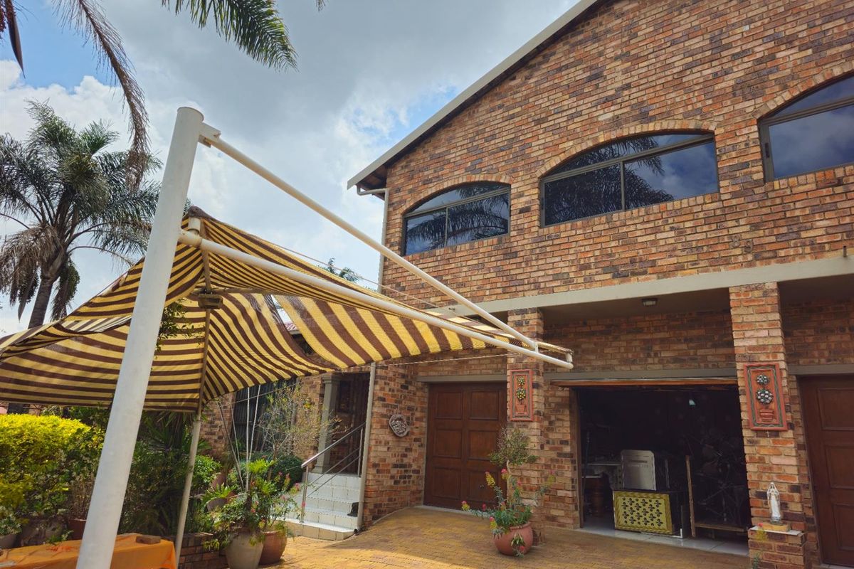 Rear view of a double-story face brick house featuring a paved patio area, retractable awning, and integrated garage access.