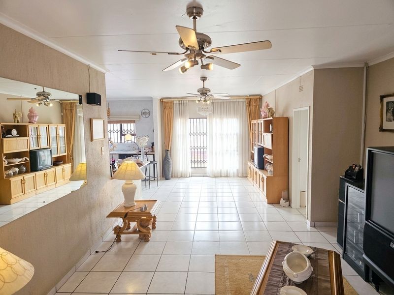 Spacious open-plan living area featuring tiled flooring, dual ceiling fans, and large sliding doors with security gates leading to the exterior.