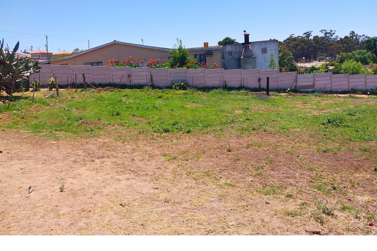 A vacant residential plot featuring a level grass and dirt surface, enclosed by a precast concrete boundary wall.