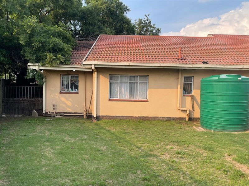 Rear view of the property featuring a tiled roof, exterior wall finishes, and a large green water storage tank situated in the garden.