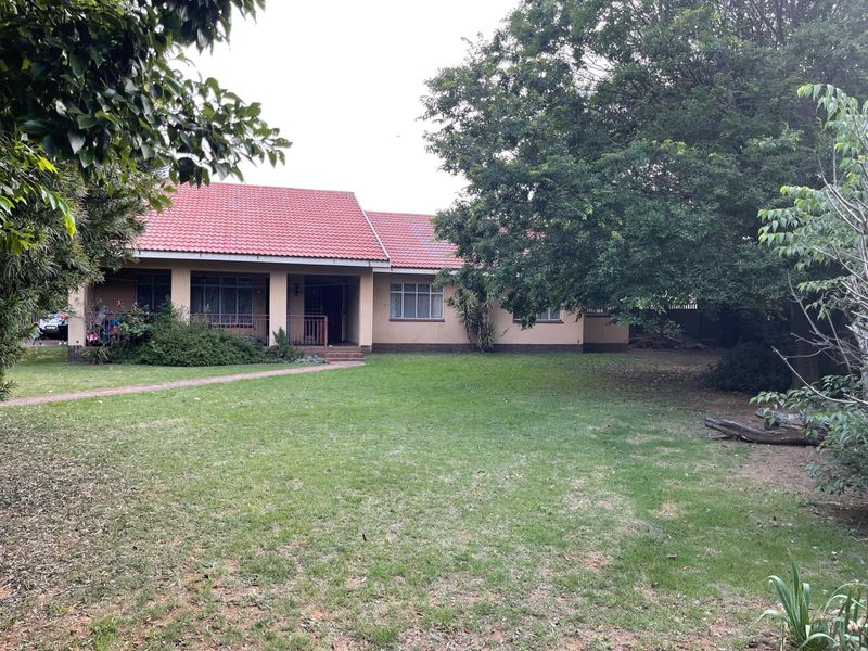 A single-story residential house featuring a tiled roof, covered front porch, and a spacious front garden with established trees and a paved walkway.