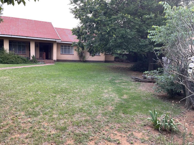 A view of the rear garden and back elevation of the house, featuring a tiled roof, covered patio area, and established trees.