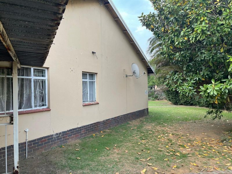Side view of the house exterior featuring brick base, plastered walls, security bars on windows, and a corrugated metal roof overhang.