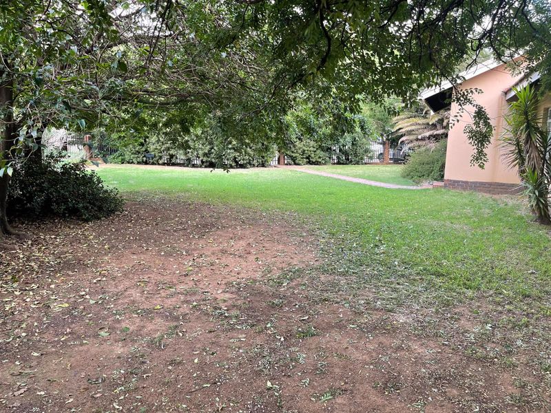 A spacious rear garden featuring a large lawn area, mature trees, and a brick pathway alongside the side of the house.