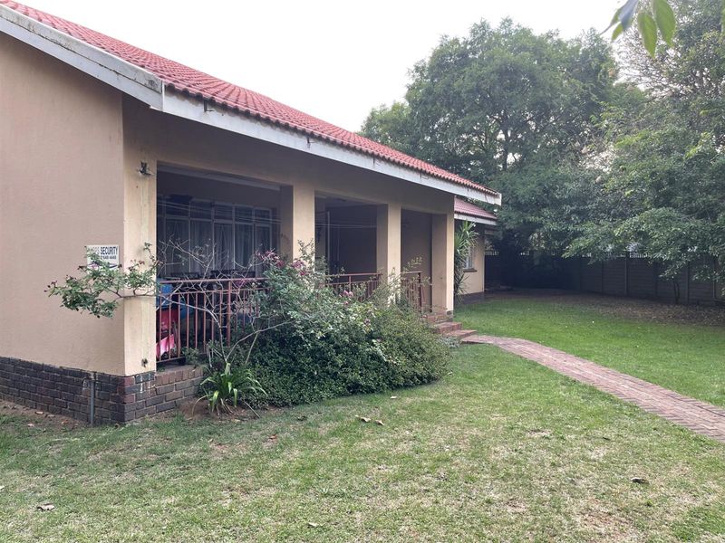 A rear view of the house featuring a covered patio area, brick pathway, and a spacious garden with mature trees.