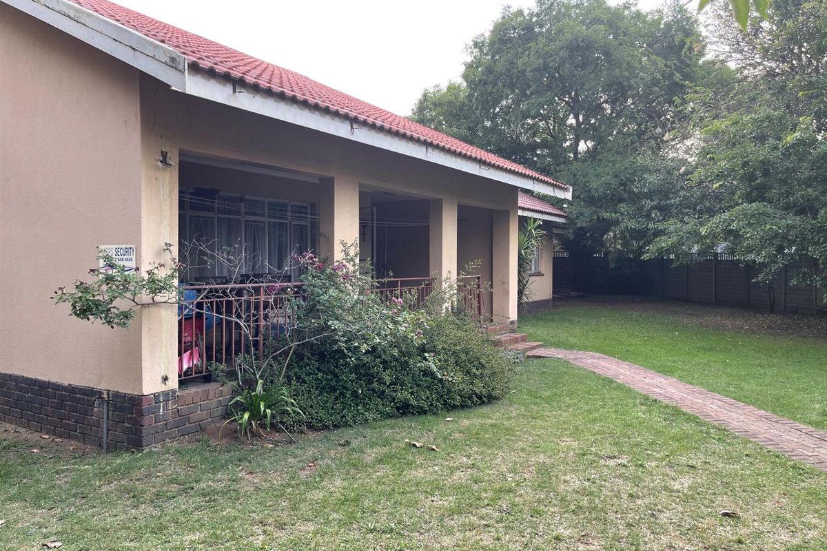 A rear view of the house featuring a covered patio area, brick pathway, and a spacious garden with mature trees.