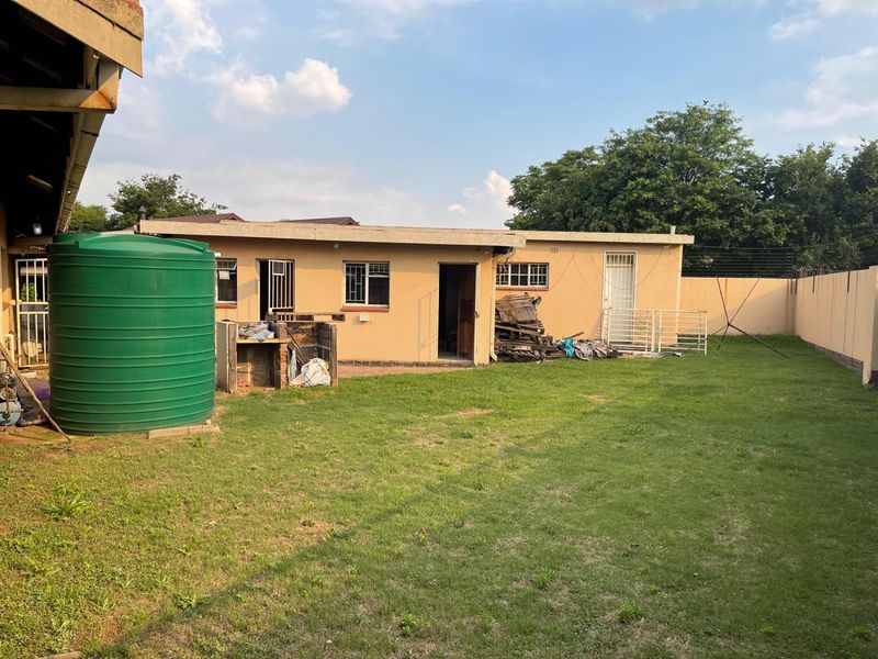 Rear view of the property featuring a large green water storage tank, a small brick structure, and a spacious backyard area.