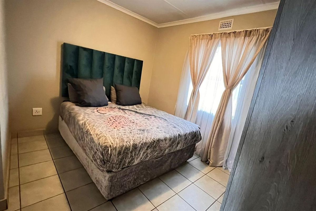 A functional bedroom featuring tiled flooring, a window with curtain tracks, and a built-in ventilation vent.