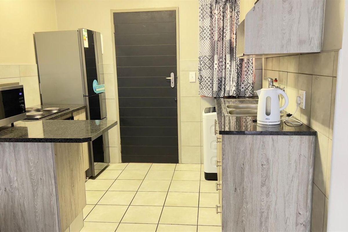 Functional kitchen featuring granite countertops, wood-look cabinetry, tiled flooring, and a built-in sink area with tiled splashbacks.
