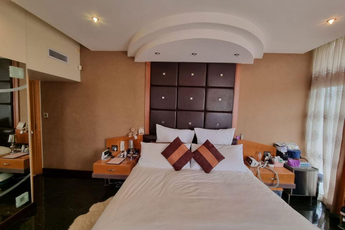A bedroom featuring a built-in upholstered headboard, recessed ceiling lighting, ducted air conditioning, and floating bedside tables with tiled flooring.
