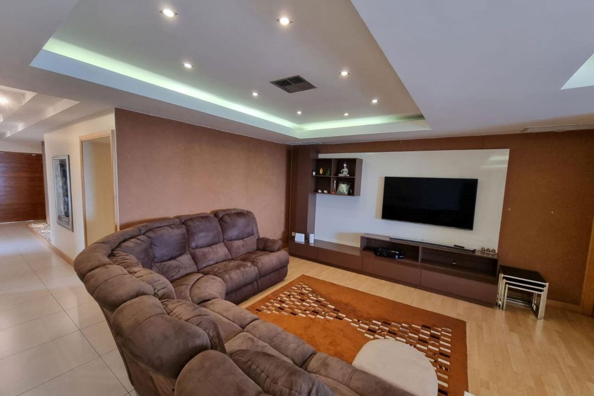 Spacious living room featuring a modern built-in media console, recessed ceiling lighting with cove accents, and a combination of tiled and laminate flooring.
