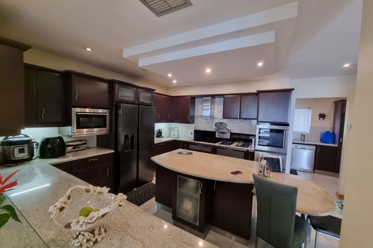 Spacious kitchen featuring dark cabinetry, granite countertops, a central island, and integrated appliances, with a connected scullery area visible in the background.