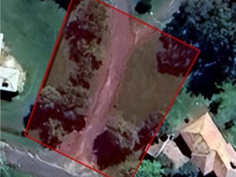 An aerial view of a vacant residential plot outlined in red, showing the land's orientation and surrounding neighborhood context.