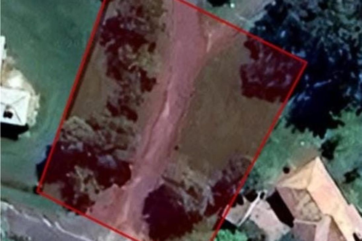 An aerial view of a vacant residential plot outlined in red, showing the land's orientation and surrounding neighborhood context.