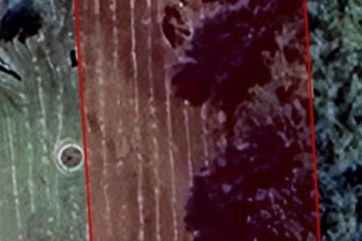 An aerial view of a vacant residential plot with a red boundary overlay indicating the property lines.