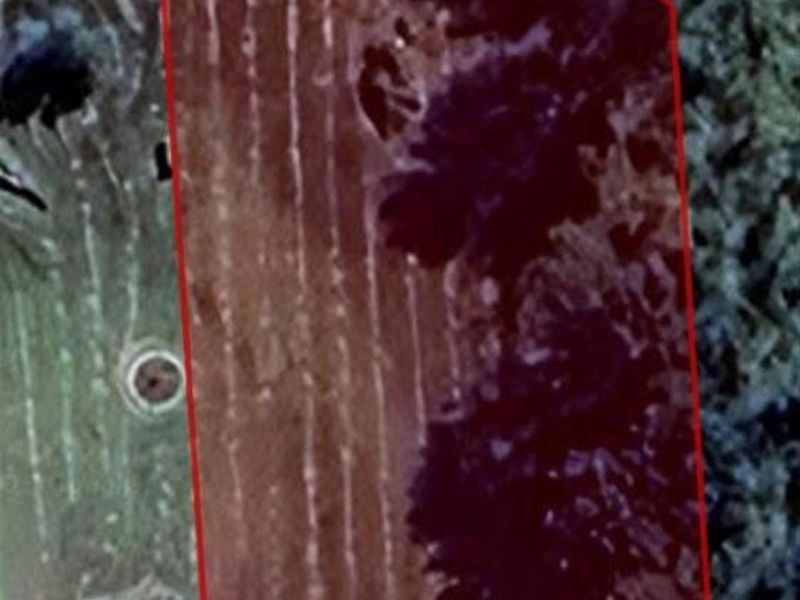 An aerial view of a vacant residential plot with a red boundary overlay indicating the property lines.