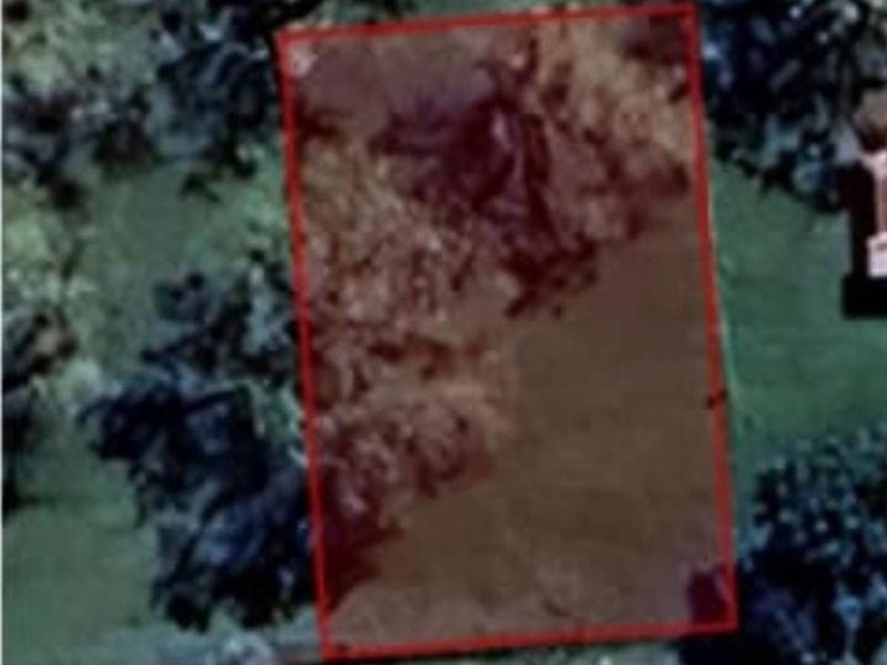 An aerial view of a vacant residential plot with a red boundary overlay indicating the property lines.