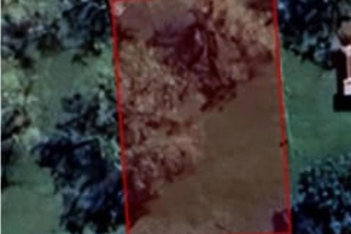 An aerial view of a vacant residential plot with a red boundary overlay indicating the property lines.