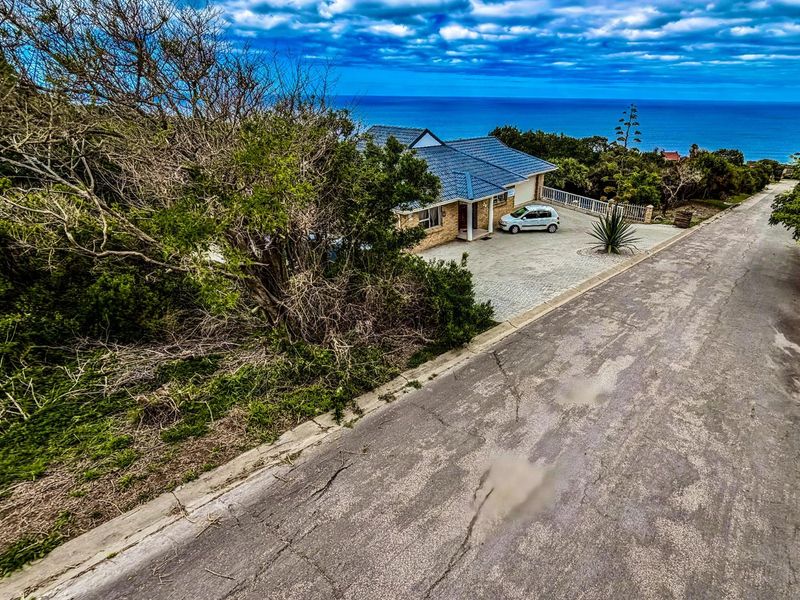 Elevated aerial view of a residential property featuring a paved driveway, tiled roof, and coastal ocean views.