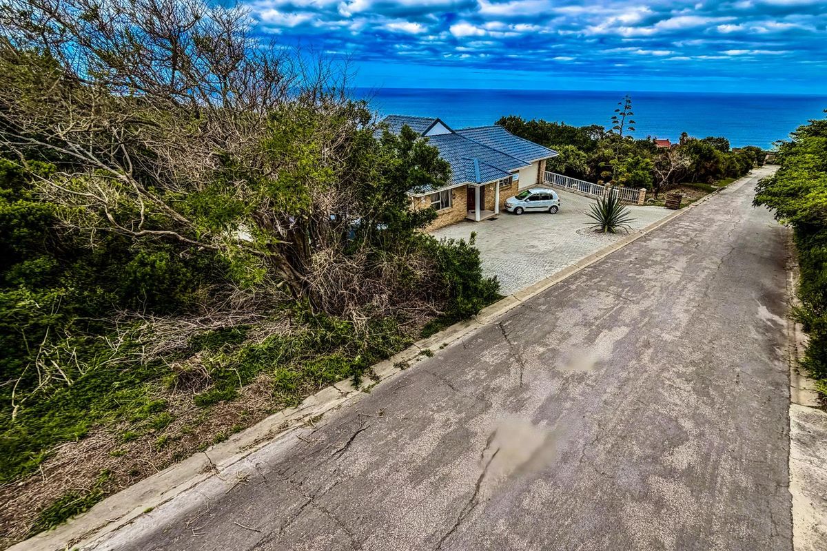 Elevated aerial view of a residential property featuring a paved driveway, tiled roof, and coastal ocean views.