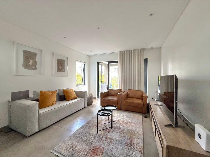 A bright and modern living room featuring tiled flooring, recessed downlighting, and a sliding glass door providing access to an outdoor area.
