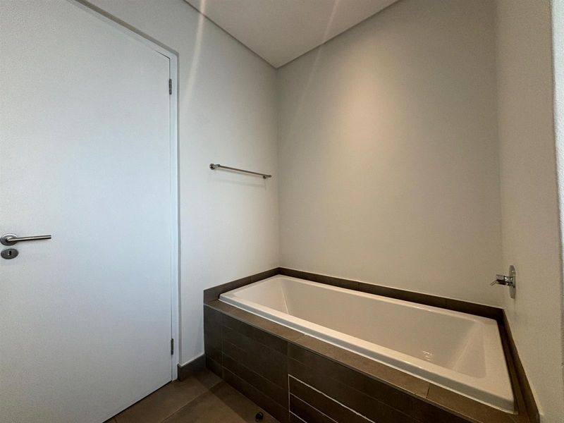 A clean and modern bathroom featuring a built-in bathtub with dark tiled surround and a wall-mounted faucet.