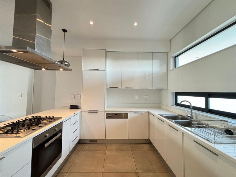 Modern kitchen featuring white gloss cabinetry, stone countertops, integrated appliances, gas hob, and stainless steel extractor fan with tiled flooring.