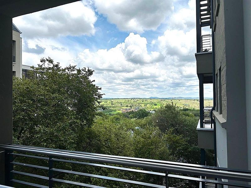 A scenic elevated view overlooking lush green landscape and distant hills, captured from a private apartment balcony with modern metal railings.