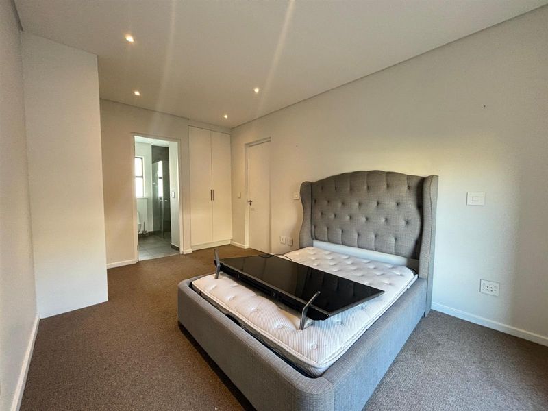 A well-maintained bedroom featuring neutral carpeting, recessed downlighting, and built-in cupboards, with direct access to an en-suite bathroom.