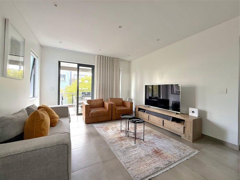 A bright and modern living room featuring neutral tiled flooring, recessed lighting, and a sliding glass door providing access to an outdoor balcony.