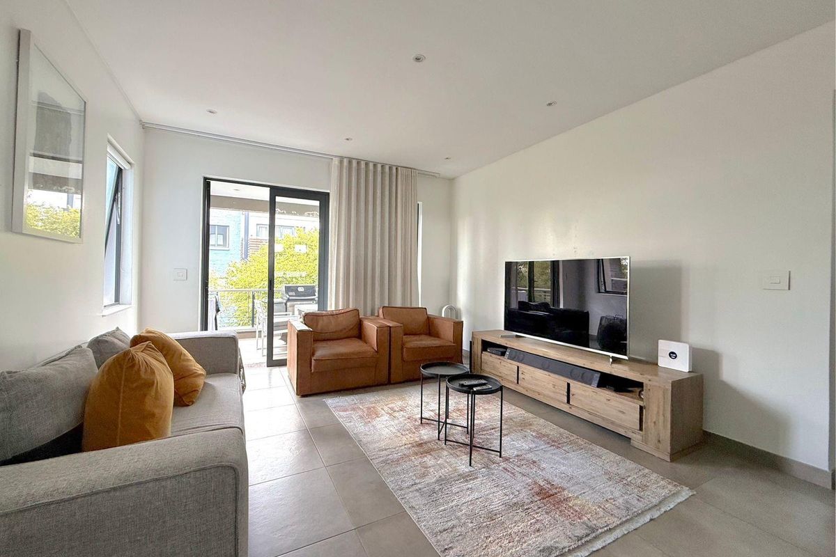 A bright and modern living room featuring neutral tiled flooring, recessed lighting, and a sliding glass door providing access to an outdoor balcony.
